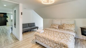 A bedroom with a large bed, a gray sofa, and a wooden floor. - Walk to Main St Stroudsburg! Pocono Townhome (Stroudsburg)