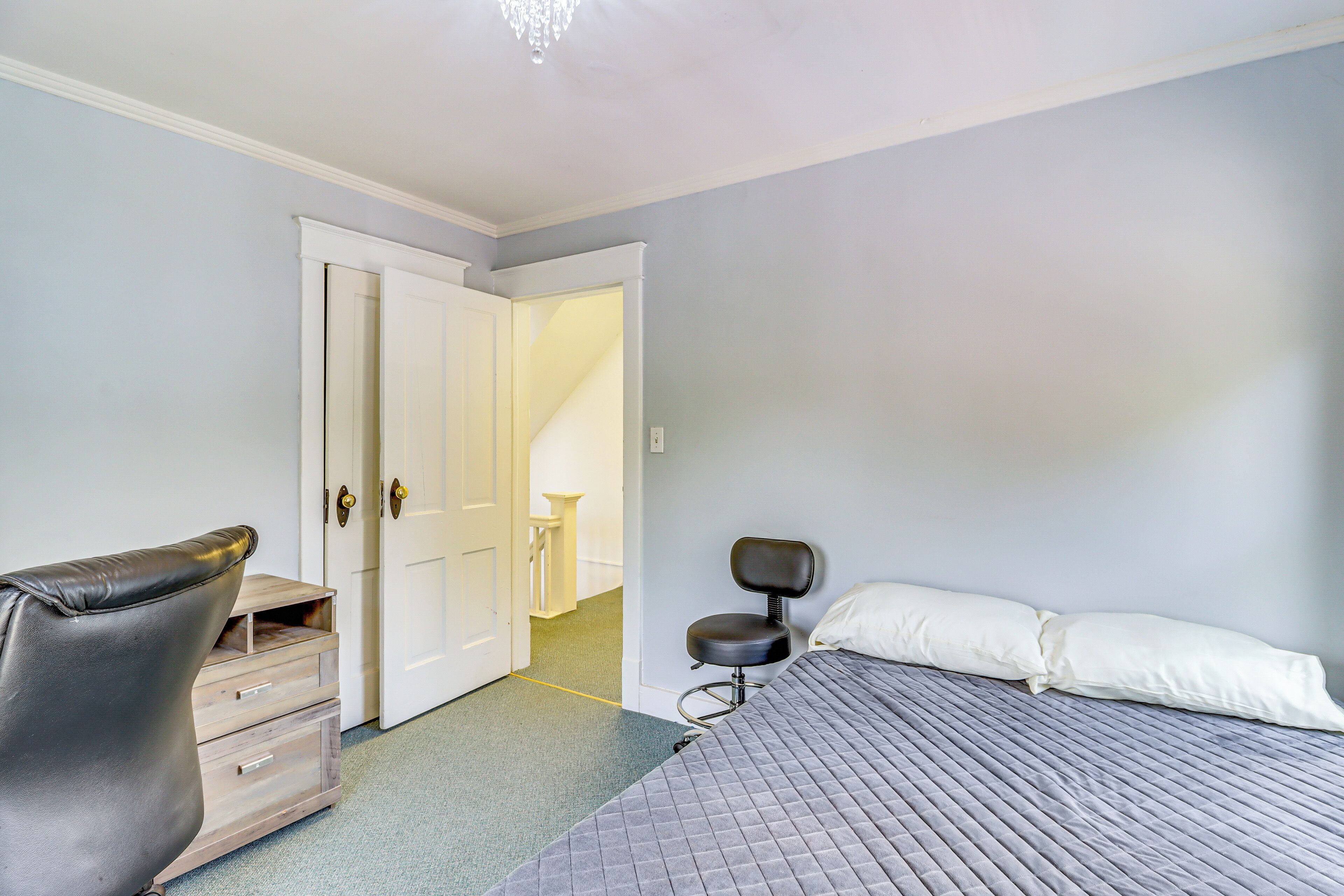 A bedroom with a bed, a chair, a dresser, and a door leading to another room.
