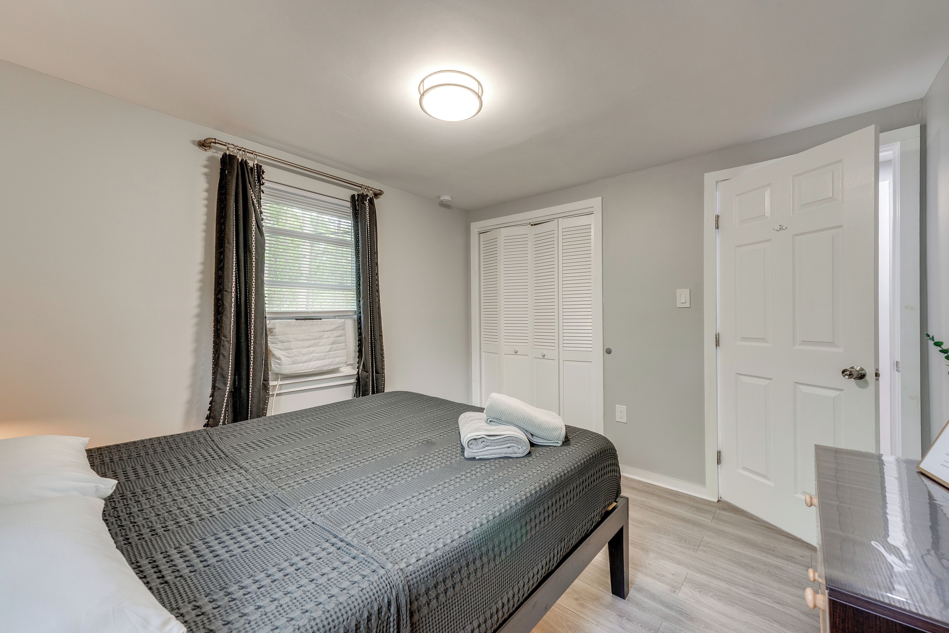 A bedroom with a bed, a bedside table, a window with curtains, and a door.