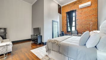 Un dormitorio moderno con una cama grande, un escritorio, un televisor y una pared de ladrillo.
