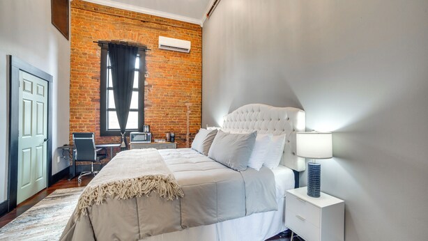 A bedroom with a brick wall, a large bed with a headboard, a desk, and a chair. - Historic Downtown Marshall: Efficient Studio Space (Marshall)
