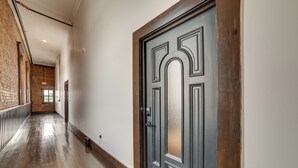 A hallway with a wooden floor, a dark door with a handle, and a brick wall on one side. - Historic Downtown Marshall: Efficient Studio Space (Marshall)