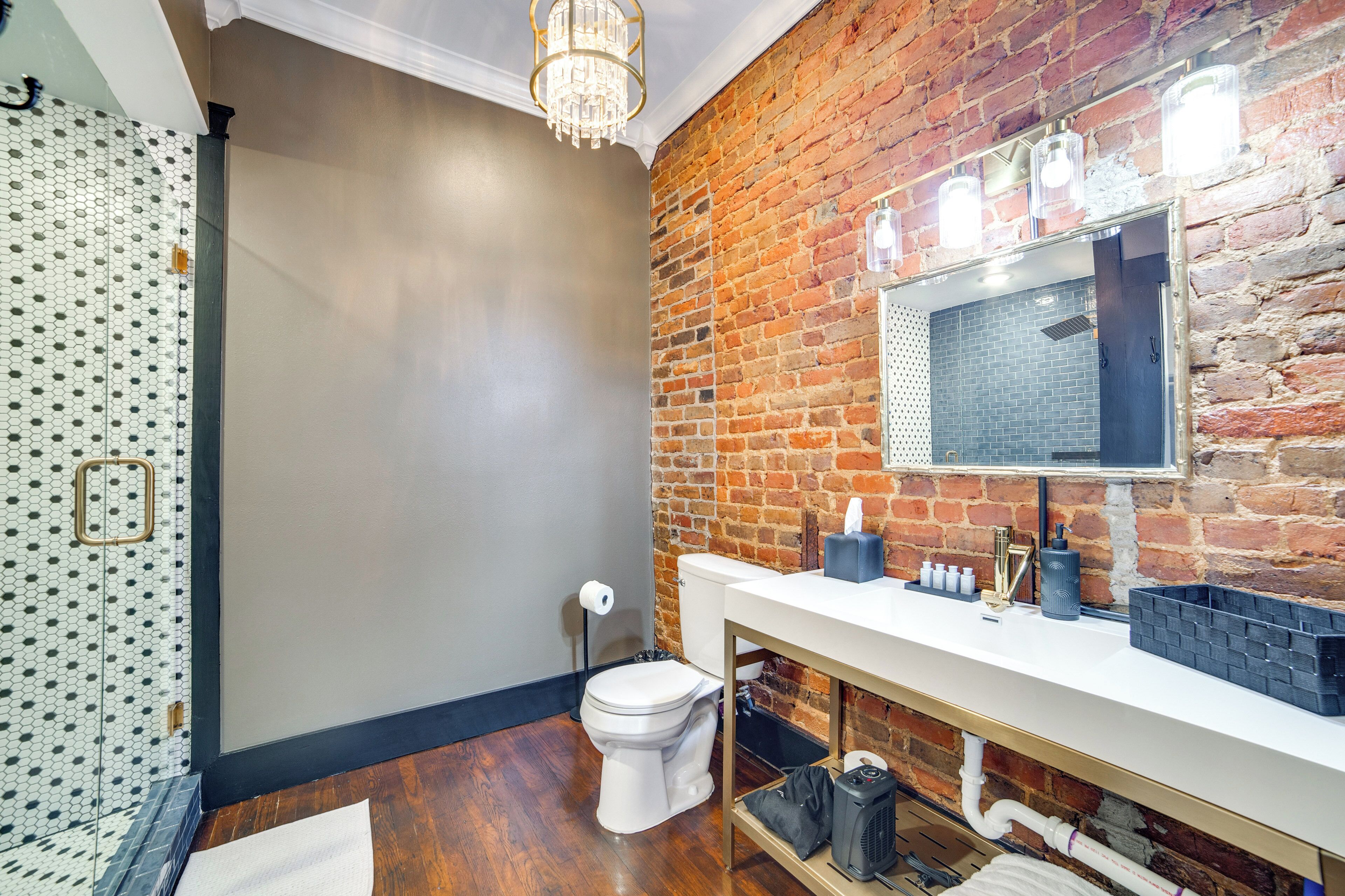 Un baño con inodoro blanco, lavabo con espejo y pared de ladrillo.
