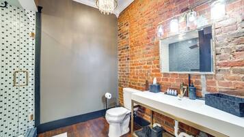 Un baño con inodoro blanco, lavabo con espejo y pared de ladrillo.