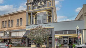 A multi-story building with a prominent clock tower, storefronts, and a tree in front.