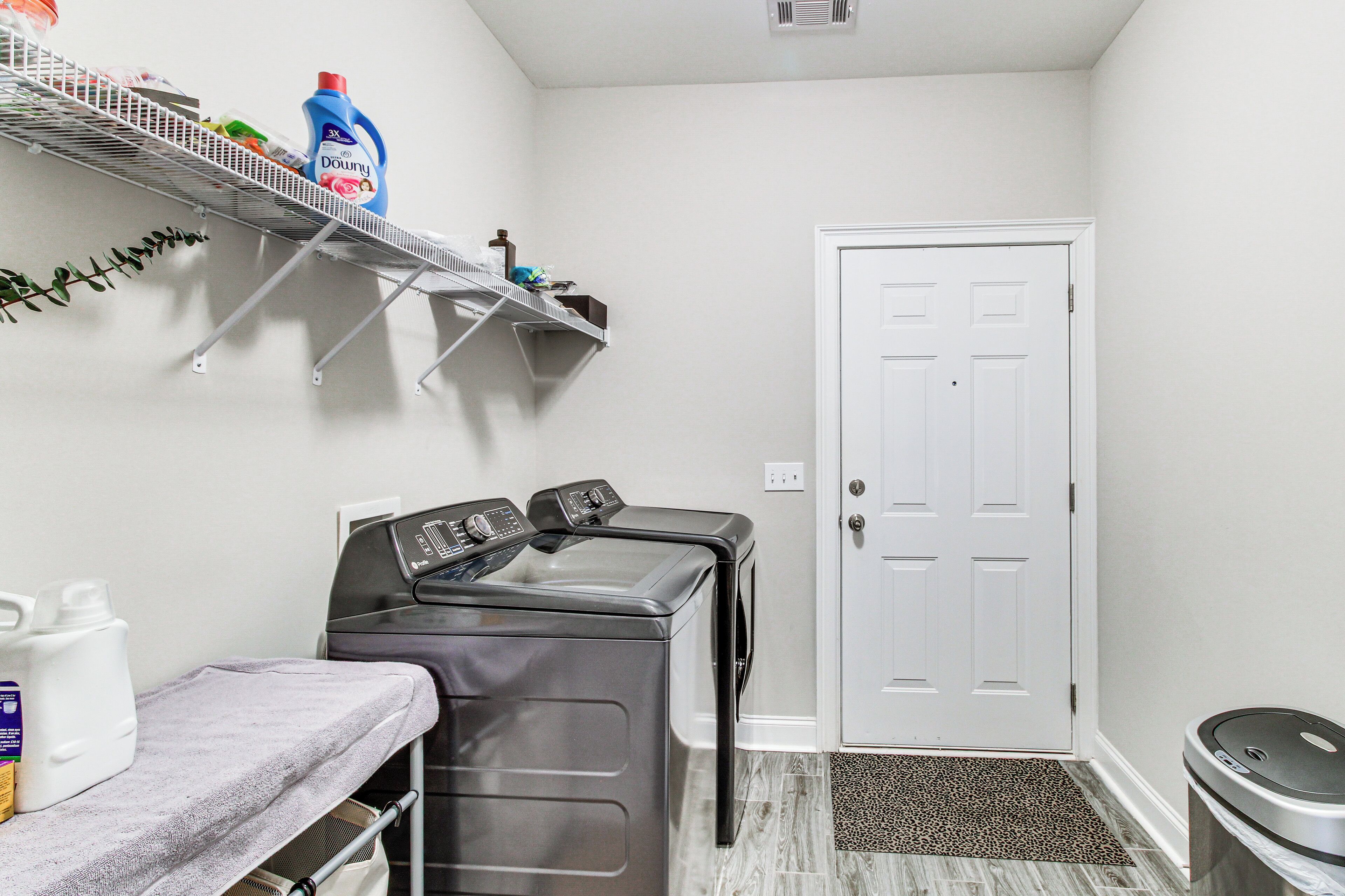 A laundry area with a washing machine, a drying rack, and shelves with laundry supplies.