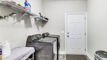 A laundry area with a washing machine, a drying rack, and shelves with laundry supplies.