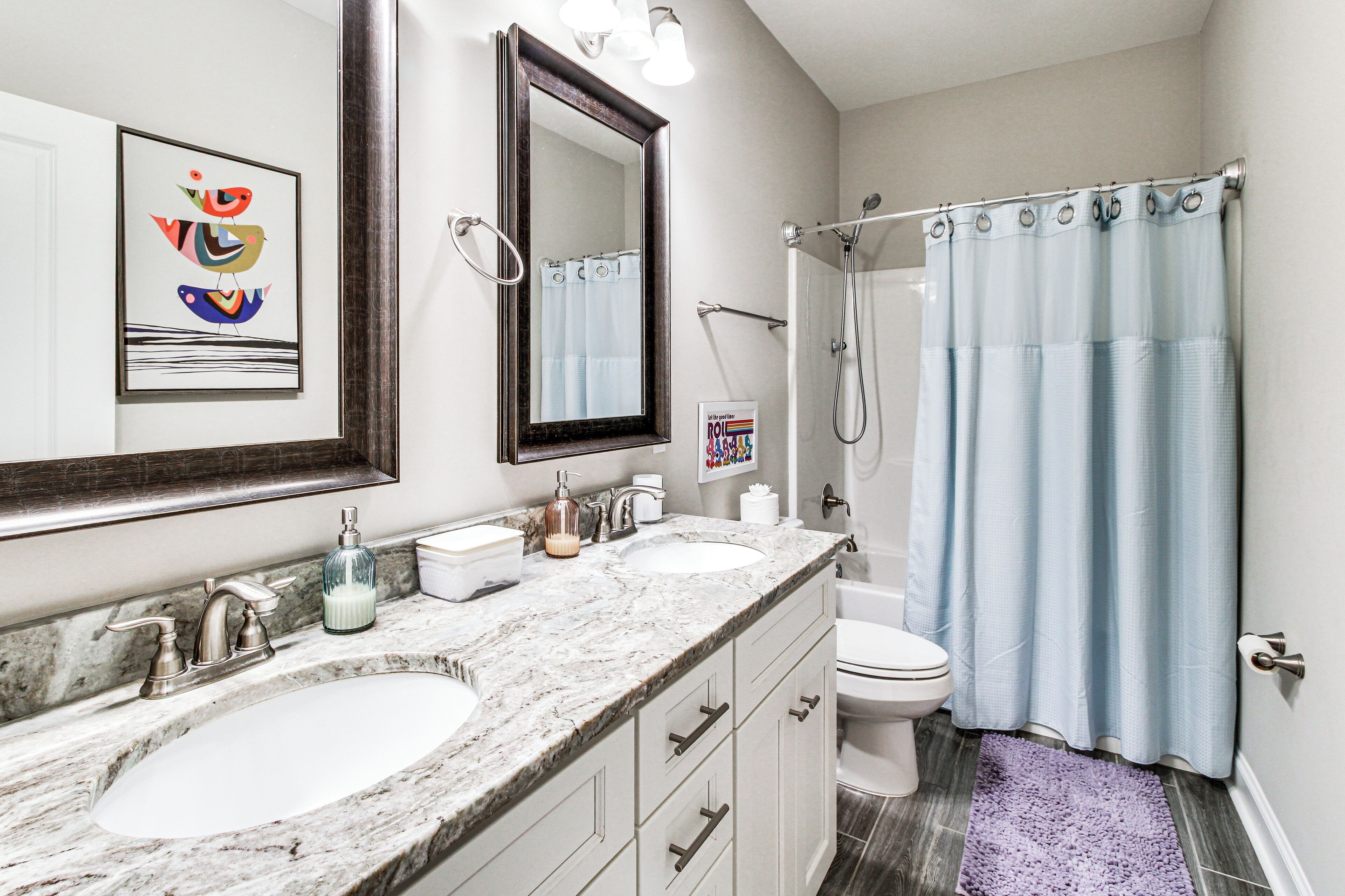 A bathroom with two sinks, a mirror, a shower, and a light blue shower curtain.