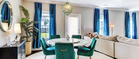 En moderne stue med et rundt spisebord, turkise stole, en beige sofa og en stor stueplante.