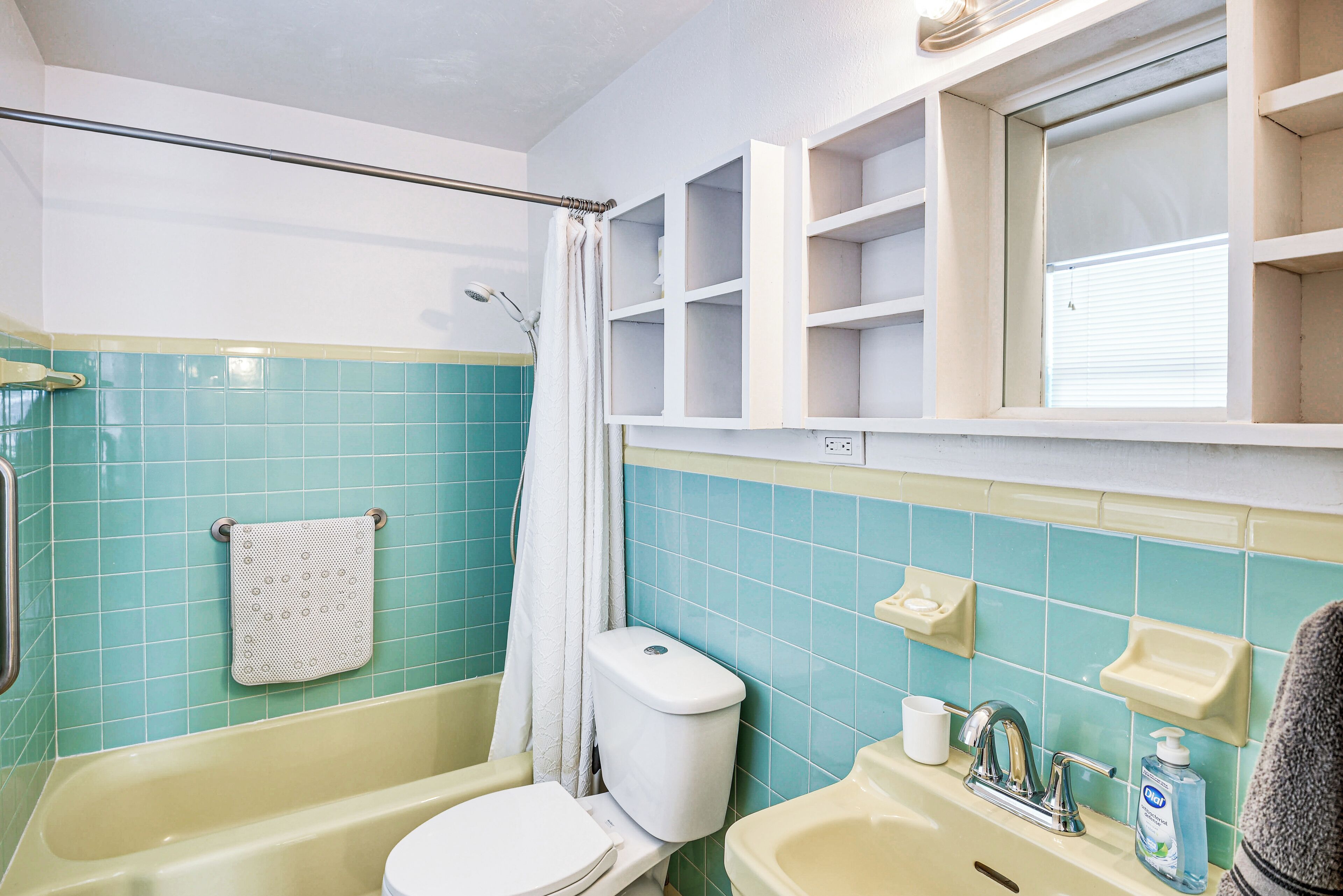 A bathroom with a bathtub, toilet, sink, and a window with shelves above.