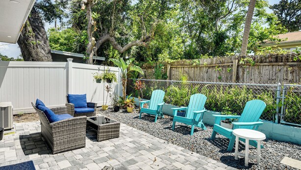 An outdoor patio area with wicker furniture, including chairs and a table, surrounded by a white fence and greenery. - Apt 3 Mi to Beach & Daytona Boardwalk Amusements! (Holly Hill)