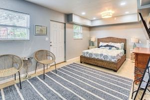 A bedroom with a bed, two wicker chairs, a small table, a rug, and a desk.