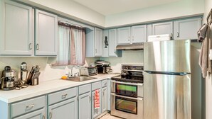 A kitchen with light blue cabinets, a stainless steel refrigerator, a stove, and a microwave.