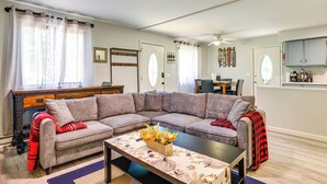 A living room with a sectional sofa, a coffee table with a floral tablecloth, and a dining area with a table and chairs.