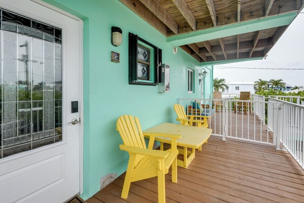 A covered deck with yellow chairs and a table, a white door, and a teal wall. - Walk to Beach: Florida Keys Gem w/ Ocean Views (Long Key)