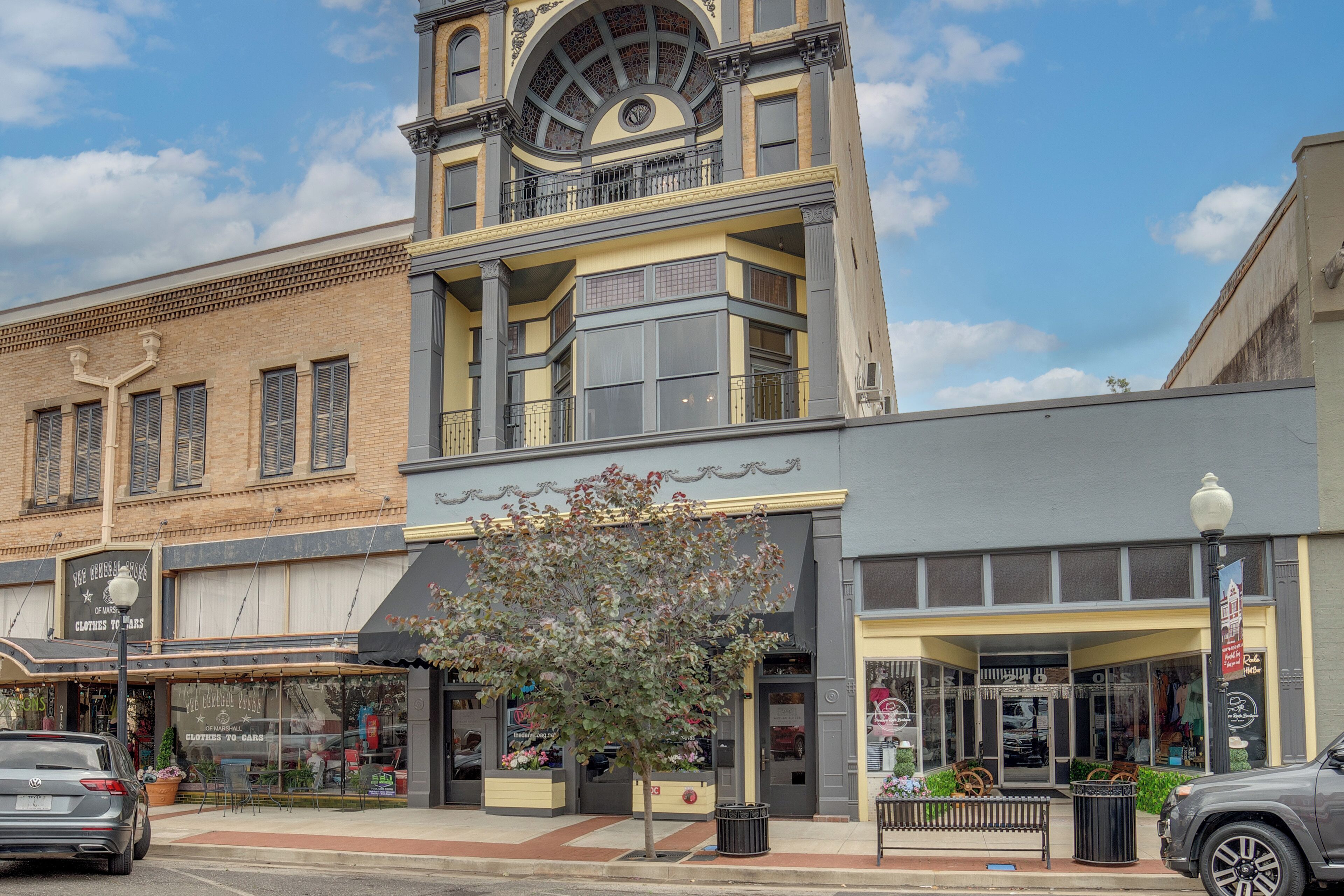 A multi-story building with a prominent clock tower, storefronts, and a tree in front.
