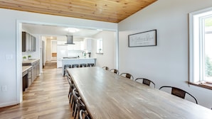 A spacious dining area with a long wooden table and chairs, a kitchen in the background, and a framed quote on the wall. - Baldwin Lakefront Home: Dock, Fire Pit & Trails! (Baldwin)