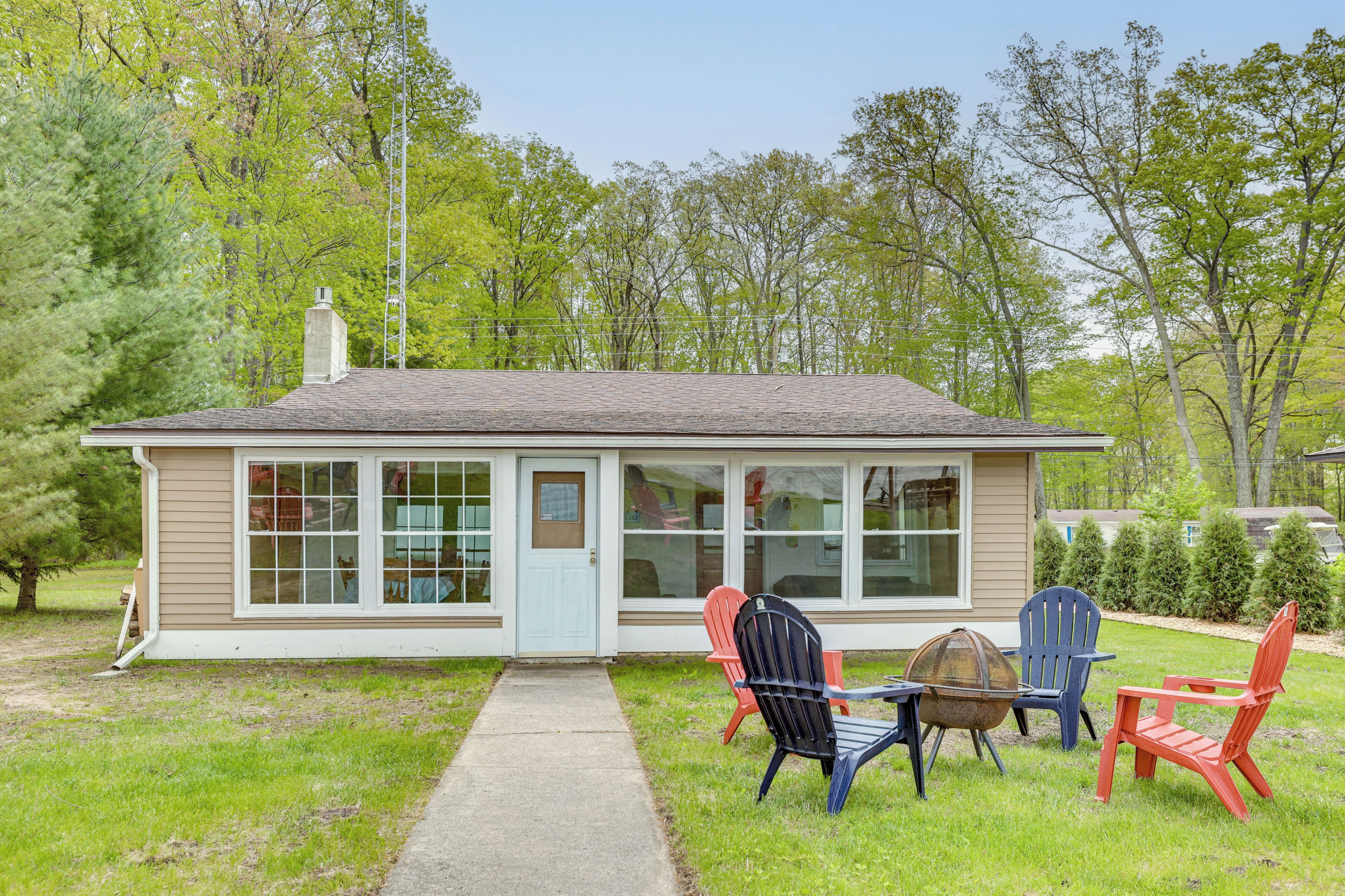 A small house with a front porch, a table, and four Adirondack chairs.