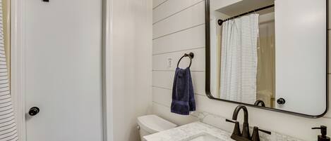 A bathroom with a white toilet, a sink with a marble countertop, a mirror, and a towel hanging on a towel ring.