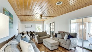 A spacious living room with a wooden ceiling, a large sofa set, and a dining area with a table and chairs. - Baldwin Lakefront Home: Dock, Fire Pit & Trails! (Baldwin)