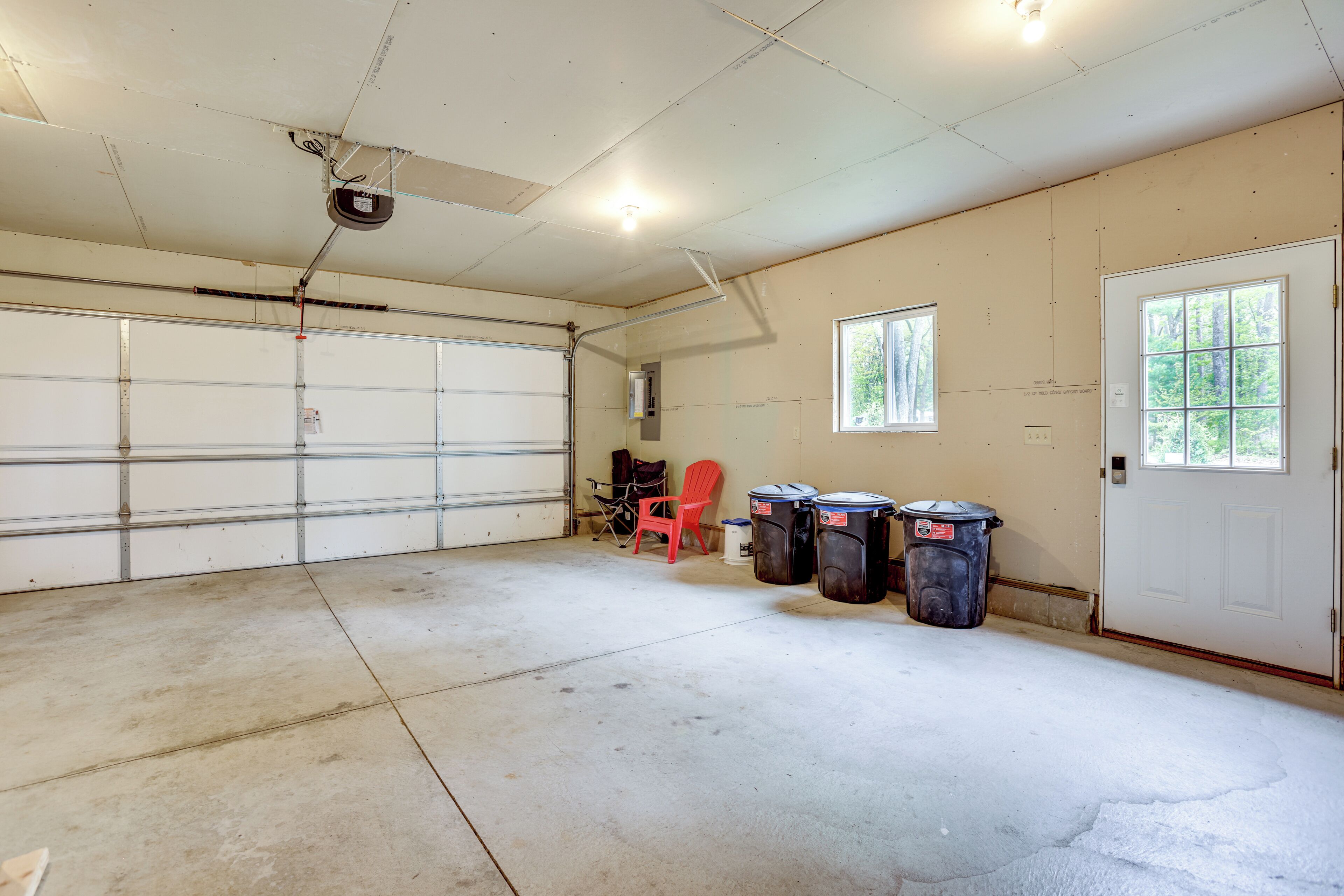 A garage with a white door, a red chair, and two trash bins.