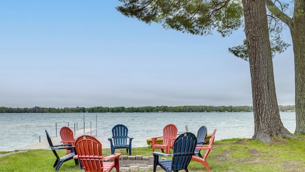A lakeside seating area with Adirondack chairs and a table. - Baldwin Lakefront Home: Dock, Fire Pit & Trails! (Baldwin)