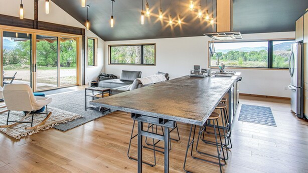 A modern kitchen with a large island, bar stools, and a view of the outdoors. - Salida Ranch Home w/ Mountain Views! (Salida)