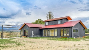 A modern two-story building with a red roof, large windows, and a dirt ground area. - Salida Ranch Home w/ Mountain Views! (Salida)