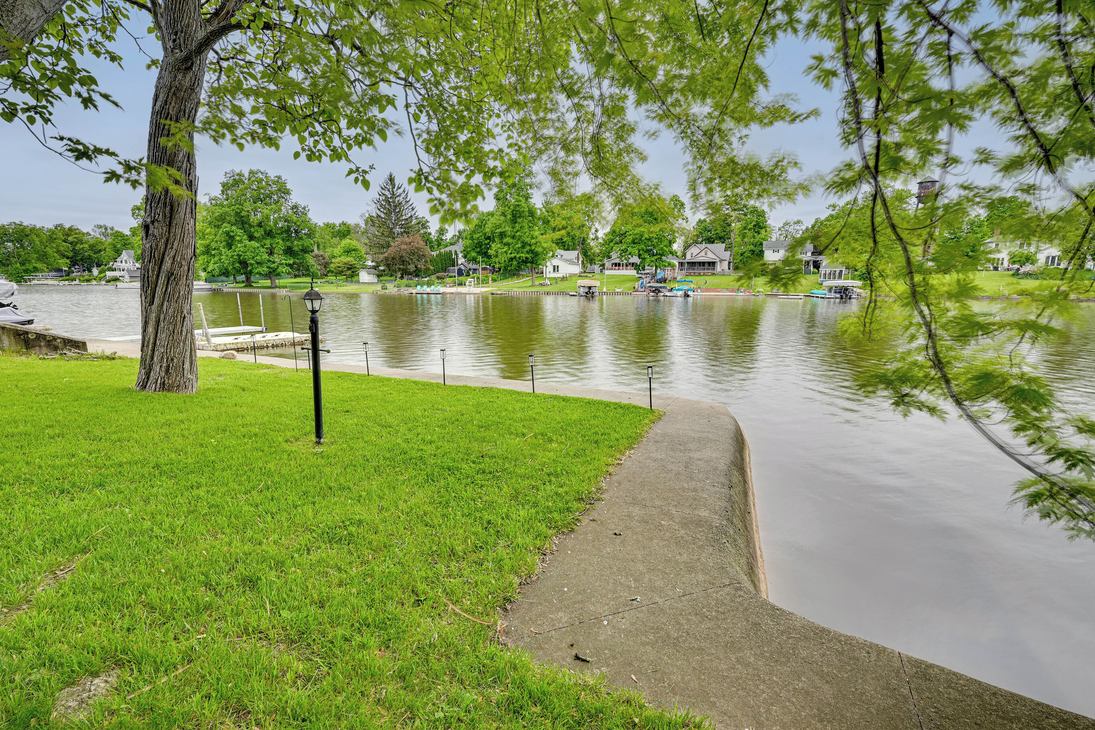 A lakeside park with a grassy area, a concrete path, and a dock with boats.