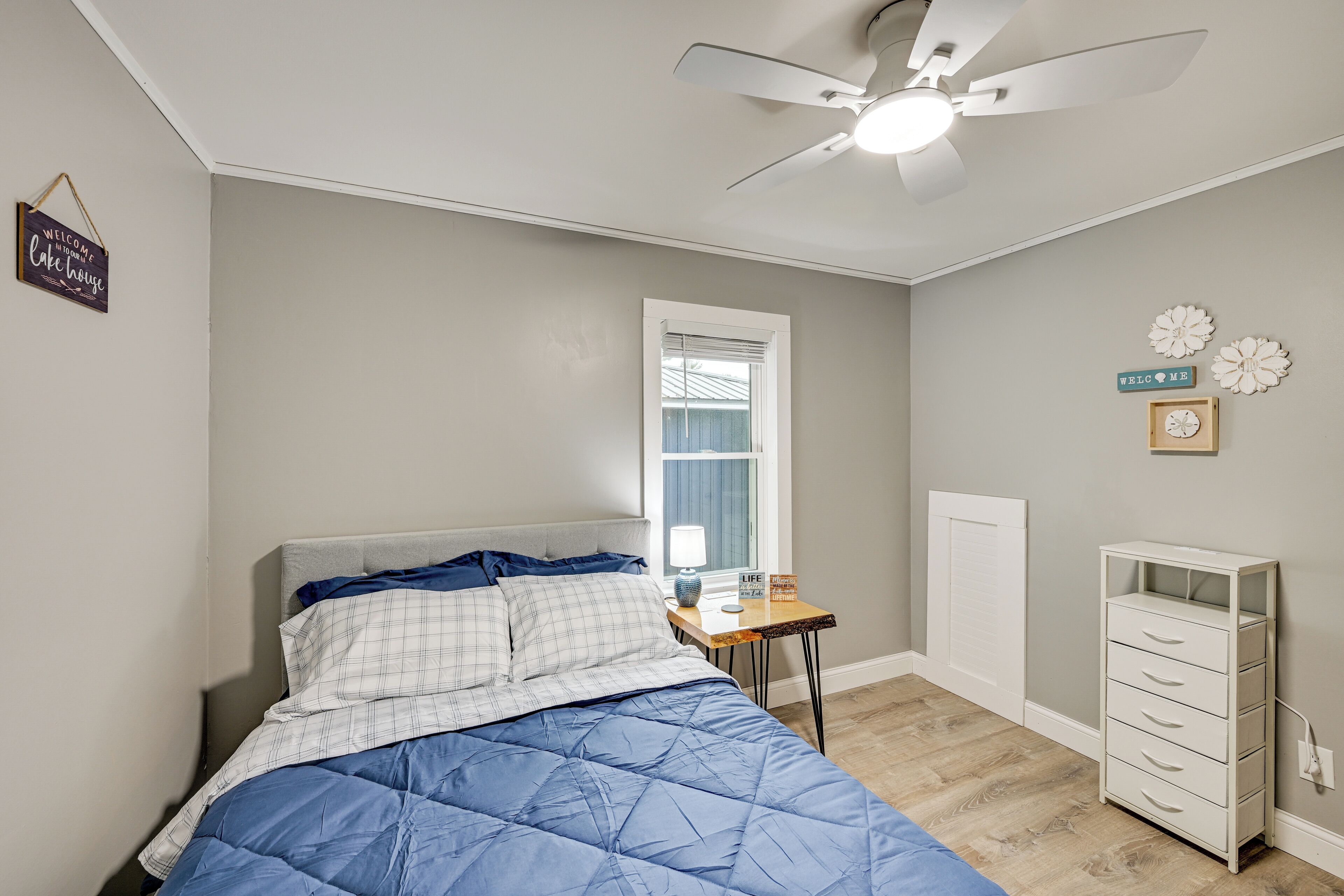 A bedroom with a bed, a desk, a dresser, a ceiling fan, and a window.
