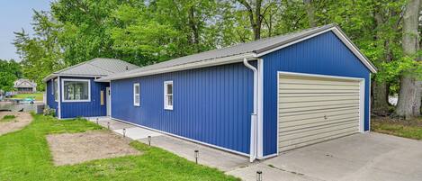 A blue single-story building with a garage, a small attached structure, and a paved driveway.