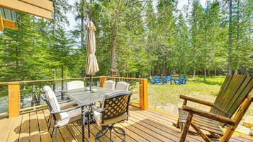 Una terraza de madera con una mesa y sillas, una silla de madera, y vista a un bosque.