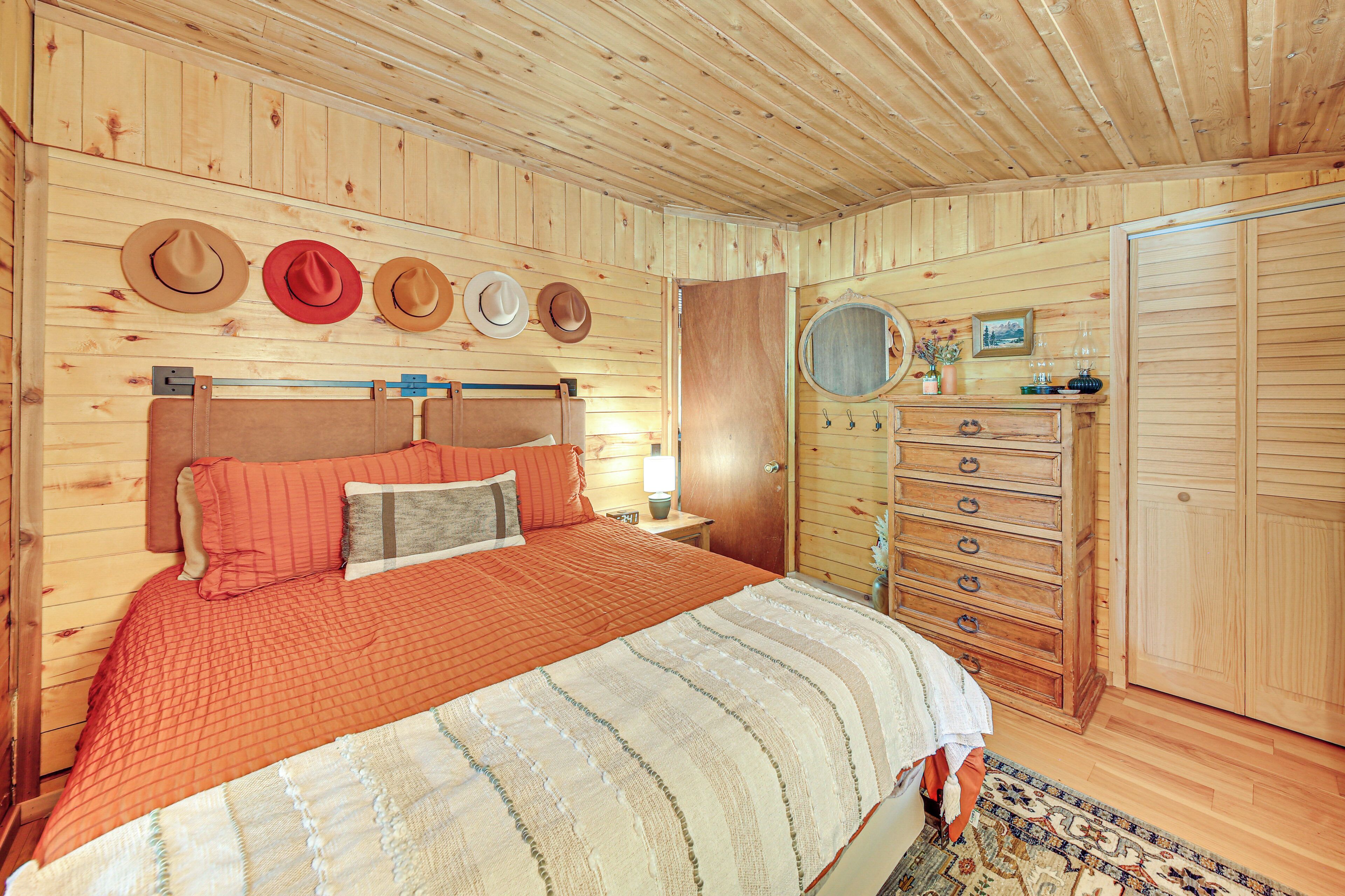 A wooden-paneled bedroom with a bed, dresser, and wall-mounted hats.