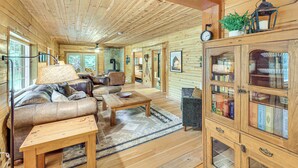 L’intérieur chaleureux d’un chalet avec un plafond en bois, un ensemble de canapés, une table à manger et une bibliothèque.