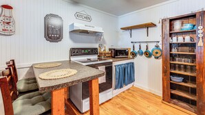 Une cuisine avec une table en bois, un fourneau, un four à micro-ondes et un meuble contenant de la vaisselle.