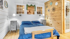 Une chambre à coucher avec un lit, deux tables de chevet, un panneau mural en bois et une fenêtre au-dessus de laquelle est affiché le mot « Grateful ».