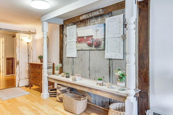 A rustic interior with a wooden bench, a welcome sign, and a vintage car painting. - Lake & Mtn Views: Vermont Couple's Retreat! (Barton)