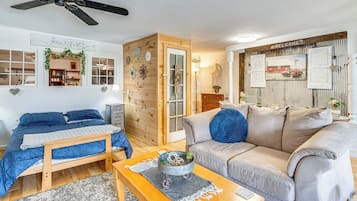A cozy living room with a bed, a sofa, a coffee table, and a wooden door leading to another room.