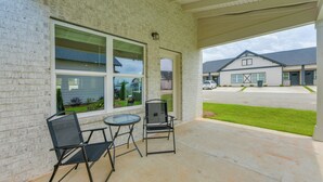 A covered patio area with two chairs and a table, a brick wall, and a view of a building with a garage.