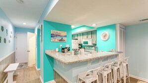 A kitchen with teal walls, a granite countertop, white bar stools, and a clock on the wall. - Heated Pool & Hot Tub! Walk to Beach & Apache Pier (Myrtle Beach)