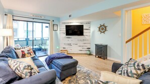 A living room with a sofa set, a flat-screen TV mounted on a wall, a wooden floor, and a staircase leading to another level. - Heated Pool & Hot Tub! Walk to Beach & Apache Pier (Myrtle Beach)