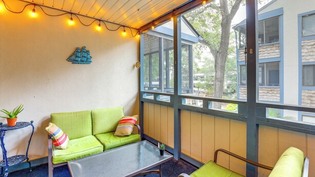 A cozy room with a green sofa, a small table, and a chair. There is a window with a view of trees and buildings outside. - Heated Pool & Hot Tub! Walk to Beach & Apache Pier (Myrtle Beach)