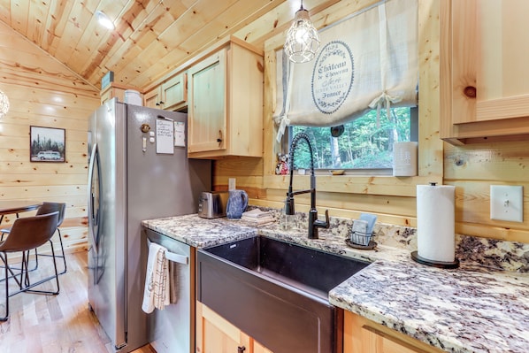 A wooden cabin kitchen with a stainless steel refrigerator, granite countertops, and a sink. - 10 Mi to Main St Murphy: Cabin w/ Covered Deck! (Murphy)