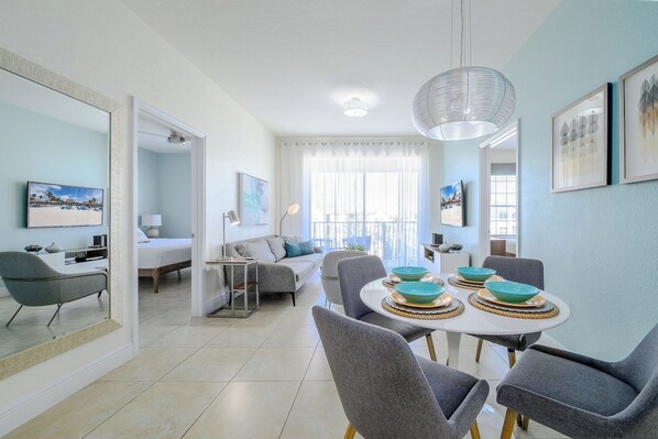 A modern living room with a dining area, a sofa, a coffee table, and a large window with curtains.