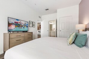 A bedroom with a large bed, a television on a wooden dresser, and a door leading to a bathroom.