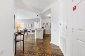 A hallway leading to a kitchen with a white door, a dining area, and a living space with a fireplace.