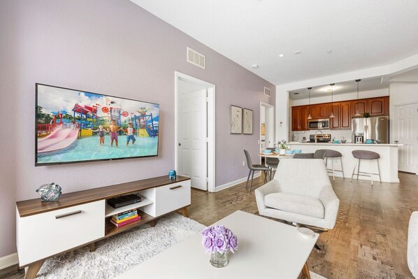 A modern living room with a flat-screen TV, a white coffee table, and a sofa.