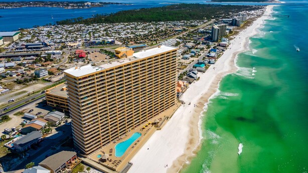 A high-rise hotel with multiple floors, a swimming pool, and a beach adjacent to the ocean.