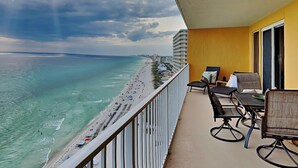 A balcony with a view of a beach and ocean, featuring outdoor seating and a railing.
