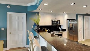 A modern kitchen with white cabinets, a stainless steel refrigerator, and a granite countertop.
